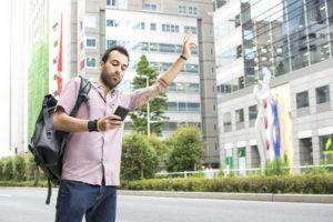 A young white italian man with tattoos, hailing a taxi whilst holding a cellphone in Tokyo.
